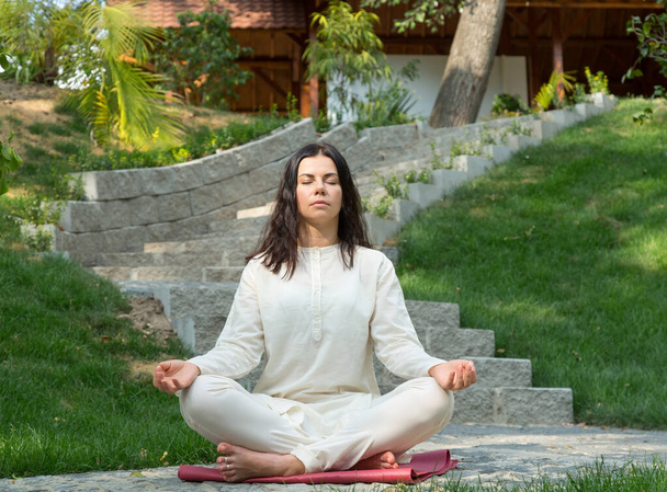 Молодая женщина сидит медитирует на свежем воздухе в природном парке
. - Фото, изображение