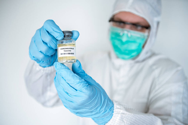 A caucasian doctor in laboratory holding a liquid vaccines for coronavirus diseases. Male scientific on protective suit with a vaccine Covid-19. Medical and health care concept, Biological hazard. - Foto, Imagem