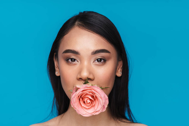 Photo of a beautiful pretty asian young woman posing isolated over blue wall background with flower. - Fotoğraf, Görsel