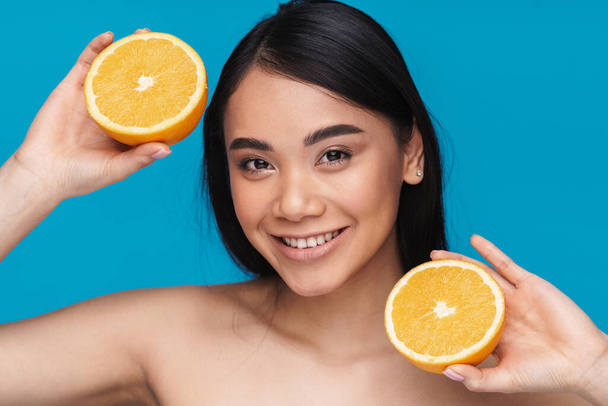 Photo of a smiling happy optimistic asian young woman posing isolated over blue wall background with orange. - Photo, Image