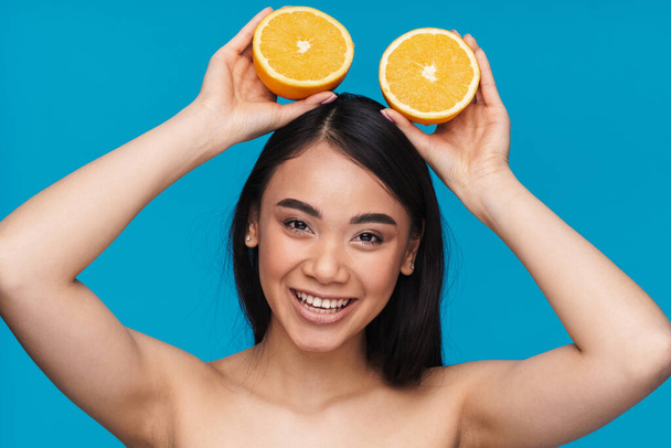 Photo of a cheerful asian young woman posing isolated over blue wall background with orange. - Photo, Image