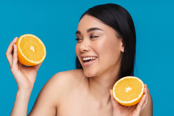 Photo of a smiling happy optimistic asian young woman posing isolated over blue wall background with orange. - Foto, Imagem