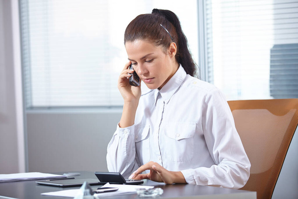επιχειρηματίας μιλάει στο έξυπνο τηλέφωνο, ενώ κάθεται στο γραφείο - Φωτογραφία, εικόνα