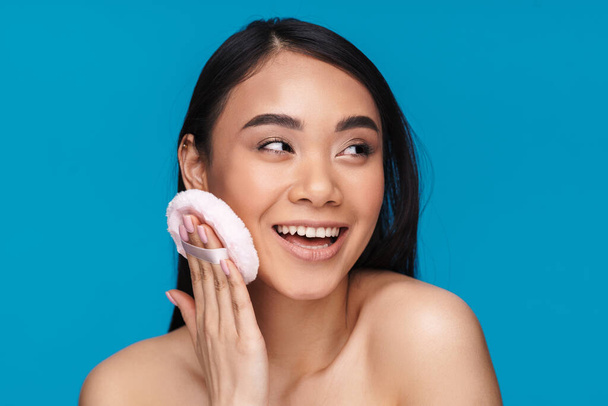 Photo of asian positive optimistic young woman posing isolated over blue wall background holding powder puff. - Φωτογραφία, εικόνα