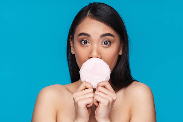 Photo of asian surprised young woman posing isolated over blue wall background holding powder puff. - Foto, Imagen