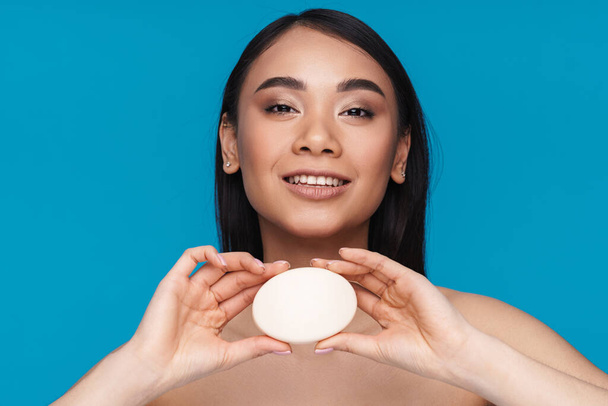 Photo of asian positive happy young woman posing isolated over blue wall background holding soap. - Zdjęcie, obraz