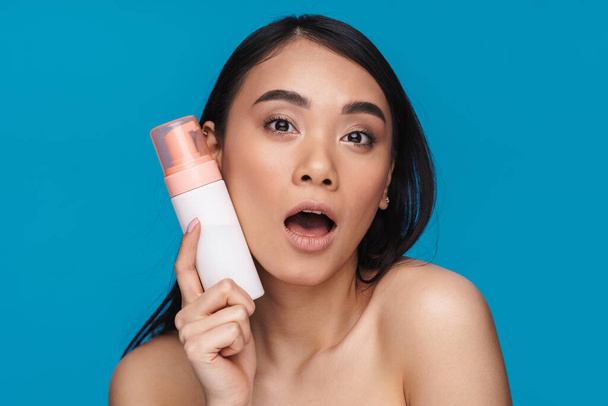 Photo of asian young woman posing isolated over blue wall background holding mousse cleansing foam. - Zdjęcie, obraz