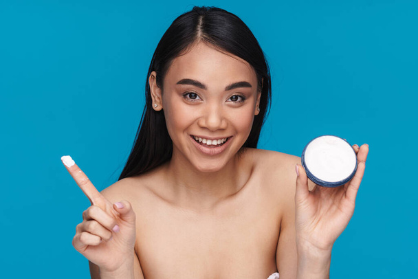 Photo of asian optimistic happy young woman posing isolated over blue wall background holding moisture cream. - Фото, зображення