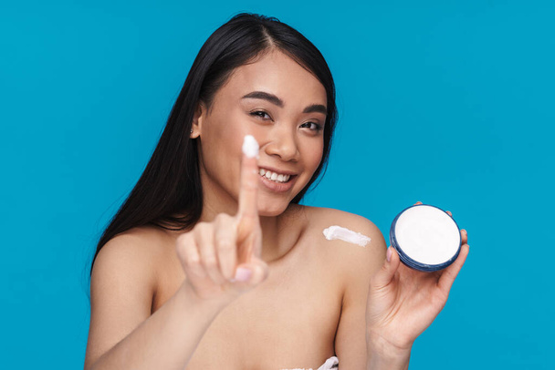 Photo of asian positive smiling happy young woman posing isolated over blue wall background holding moisture cream. - Фото, изображение