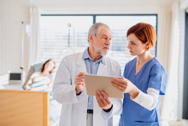 Doctor and nurse with tablet discussing issues in hospital room. - Photo, Image
