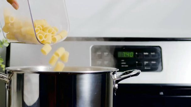 Rauwe pasta macaroni in de pot doen. Pasta in steelpan gieten - Foto, afbeelding