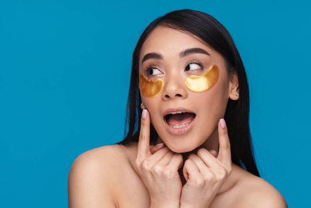 Photo of asian happy positive optimistic young woman posing isolated over blue wall background take care of undereye skin with patches. - Φωτογραφία, εικόνα