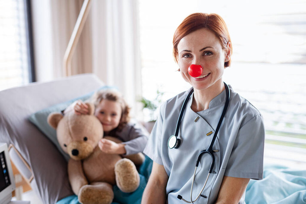 Friendly female doctor examining small girl in bed in hospital. - Zdjęcie, obraz