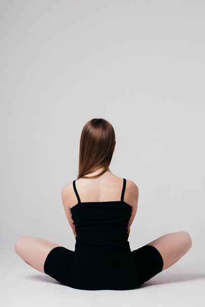 A young girl in black sportswear sits with her back to the camera on a white background and meditates - Photo, Image