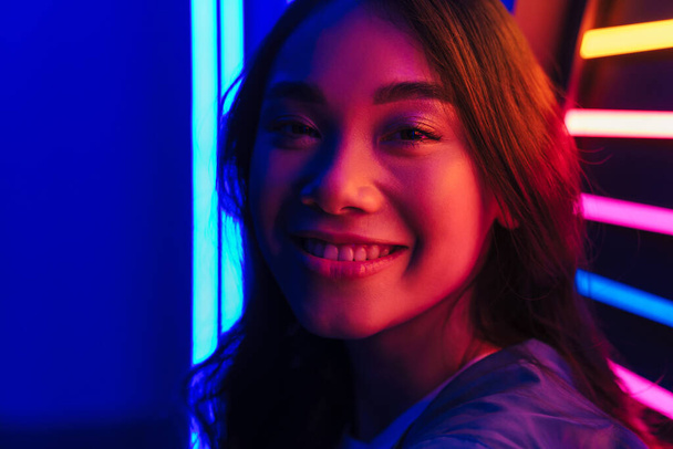 Image of asian happy positive smiling pretty beautiful young woman posing over neon lights. - Foto, Imagem