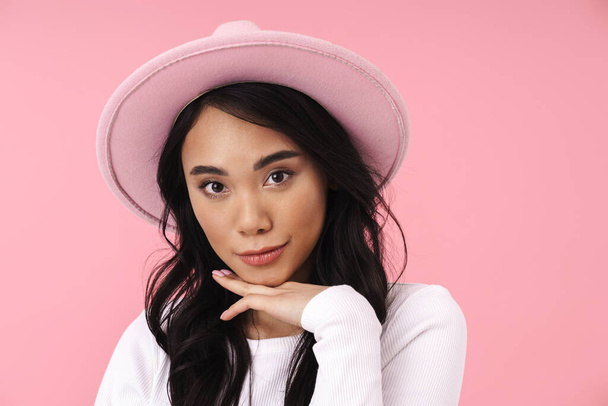 Image of young brunette asian woman wearing hat smiling and looking at camera isolated over pink background - Foto, imagen