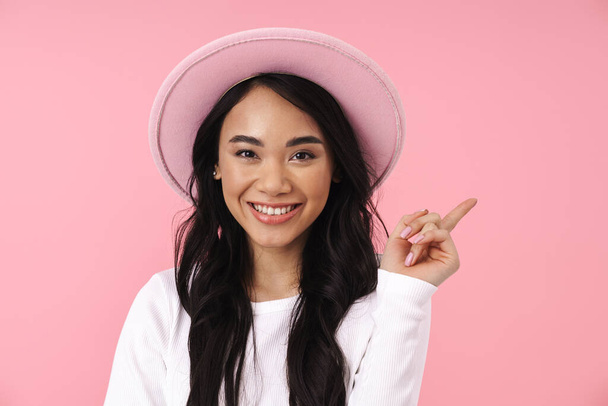 Image of young brunette asian woman in casual clothes pointing finger aside at copyspace isolated over pink background - Valokuva, kuva