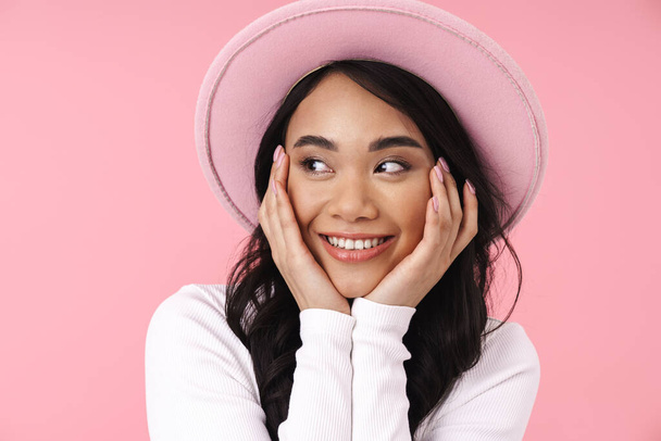 Image of young brunette asian woman wearing hat smiling at camera isolated over pink background - Foto, Bild
