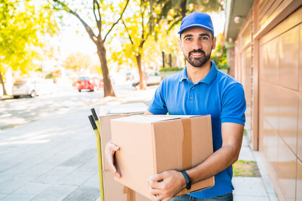Portrait of a delivery man courier with cardboard boxes in hands outdoors. Delivery and shipping concept. - Zdjęcie, obraz