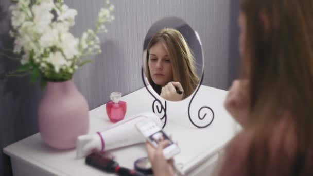 Mladá krásná žena drží štětec aplikovat červeň prášek a pomocí smartphonu - Záběry, video