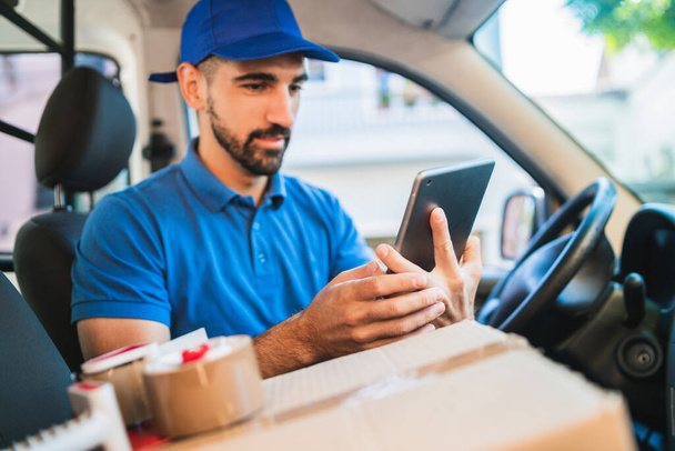 Retrato de un conductor repartidor usando tableta digital mientras está sentado en la furgoneta. Servicio de entrega y concepto de envío. - Foto, imagen