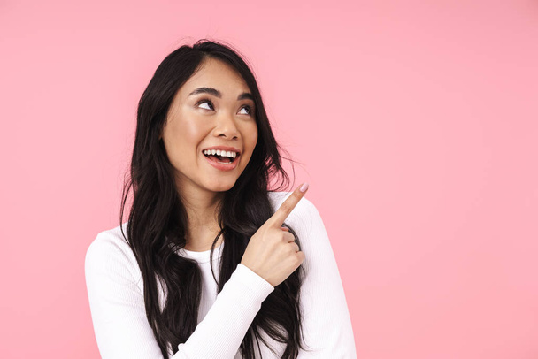 Image of young brunette asian woman in casual clothes smiling and pointing fingers aside isolated over pink background - Fotoğraf, Görsel