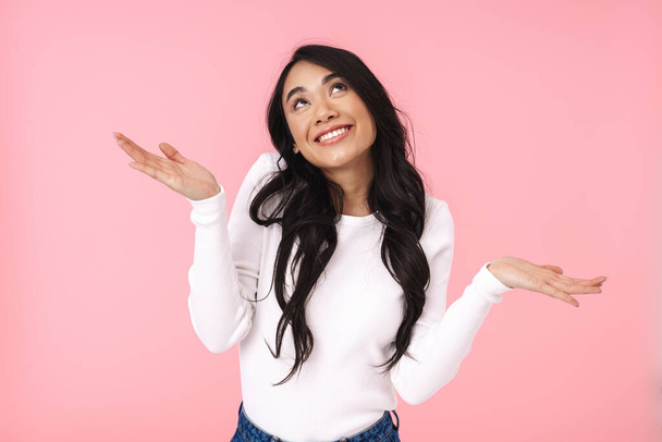 Image of young brunette asian woman in casual clothes smiling and looking upward at copyspace isolated over pink background - Valokuva, kuva