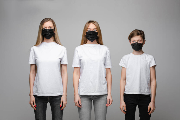 Portrait of two handsome girls with long fair hair and a young boy with black medical masks on their faces isolated on grey background - Фото, зображення