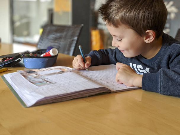 Çalışkan küçük bir çocuğun portresi. Masada oturmuş ödevlerini yapıyor. - Fotoğraf, Görsel
