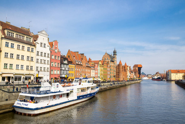 Gdansk, Poland, April 15, 2018: White tourist boat ship on Motlawa river water, typical colorful houses buildings and Zuraw Crane at Long Bridge embankment promenade street in historical town centre - Photo, Image
