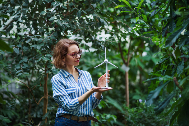 Young woman standing in botanical garden, holding windmill model. - Fotografie, Obrázek