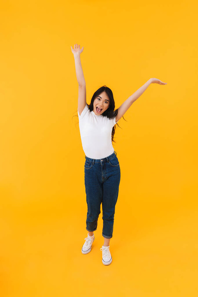 Full length image of young brunette asian woman wearing casual clothes smiling and having fun isolated over yellow background - Foto, Bild