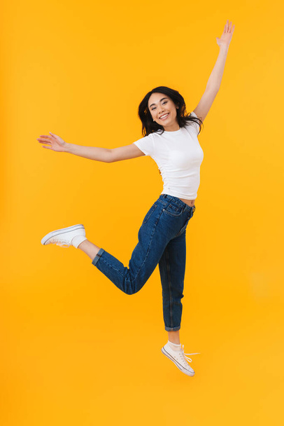 Full length image of young brunette asian woman wearing casual clothes smiling and having fun isolated over yellow background - Foto, afbeelding