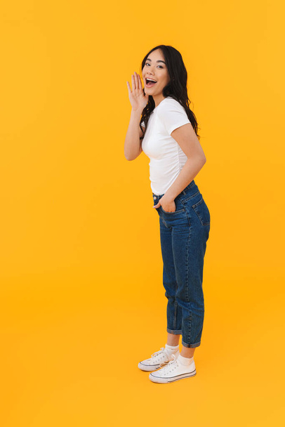 Full length image of young brunette asian woman calling or screaming isolated over yellow background - Φωτογραφία, εικόνα
