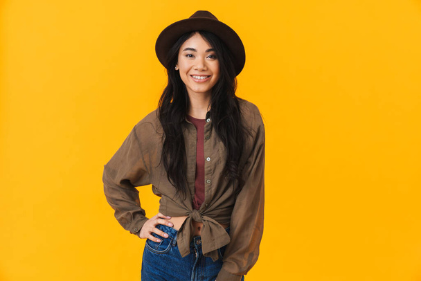 Image of young brunette asian woman wearing hat smiling and looking at camera isolated over yellow background - Φωτογραφία, εικόνα