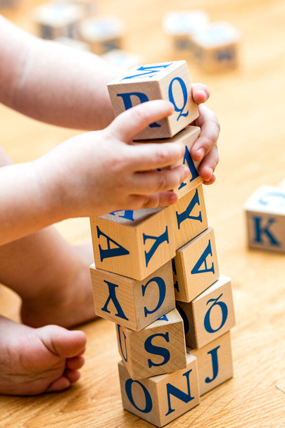 Ababy is playing with wooden cubes with colored letters on the wooden floor of the background - Foto, immagini