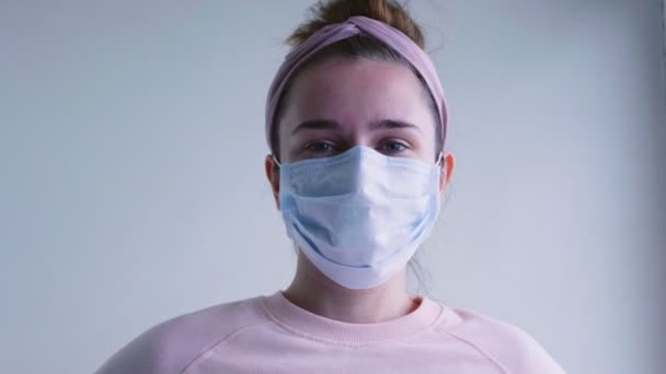医療用マスクの若い女性が窓の外を見て、医療用マスクを脱いで笑顔。Covid-19のコンセプト。コロナウイルスのパンデミックと隔離の終わり. - 映像、動画