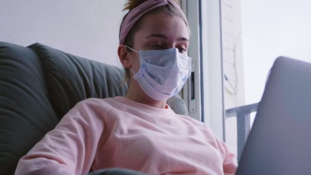 Funny young woman trying to drink a coffe through the protective mask while working from home. Woman in medical mask with laptop. Coronavirus, 2019-nCoV, Covid-19 . Quarantine and self isolation. - Video