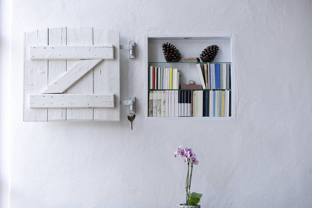 Półka na książki z ładnym wystrojem i białą drewnianą marną okiennicą w białej fakturowanej ścianie z przestrzenią na ksero i piękną orchideą - Zdjęcie, obraz