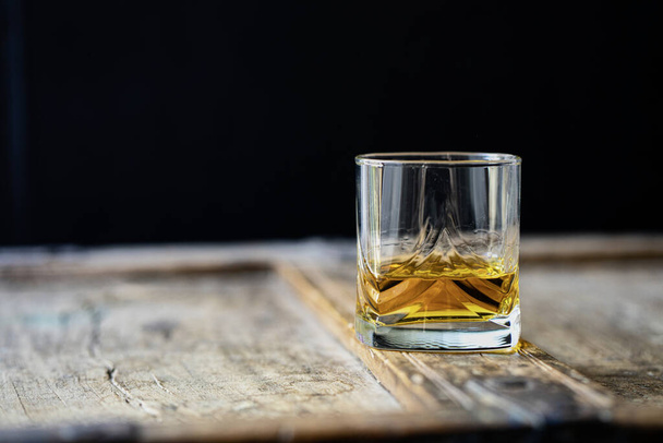 Primer plano de un whisky dorado brillante en un vaso sobre un viejo barril de madera con un fondo negro
 - Foto, Imagen