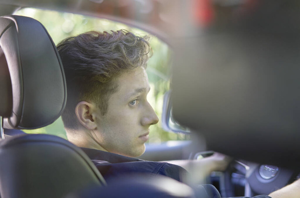 Крупный план молодого красивого водителя, сидящего в машине и смотрящего в сторону, сфотографированного сзади
                       - Фото, изображение