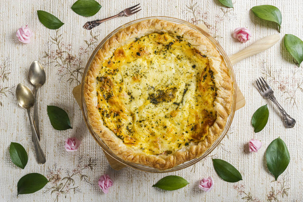 Top view of a delicious quiche surrounded by flowers and leaves in a fresh, spring setting. Healthy food. Cooking at home. - Photo, Image