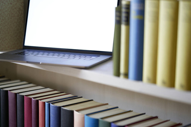 Zbliżenie laptopa z pustym ekranem stojącym w biblioteczce z dokładnymi kolorowymi okładkami książek - Zdjęcie, obraz