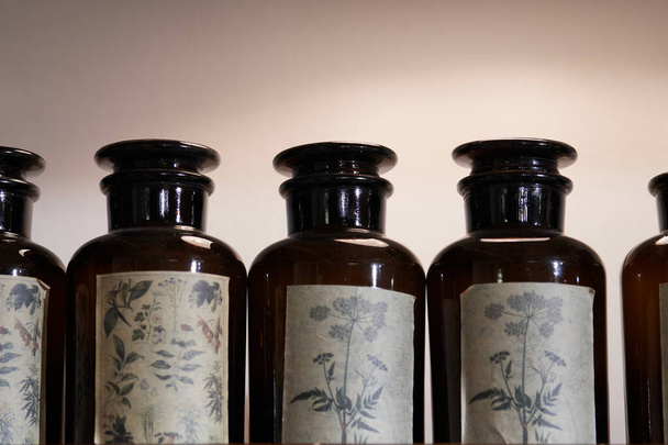 Uma linha de jarros de boticário de vidro marrom vintage com etiquetas usadas exibindo desenhos à base de plantas
 - Foto, Imagem