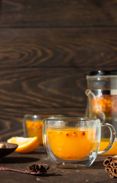 Colorful hot spicy sea buckthorn tea with cinnamon, anise and honey in glass cup on dark brown concrete background, selective focus. Vitamin drink. - Photo, image