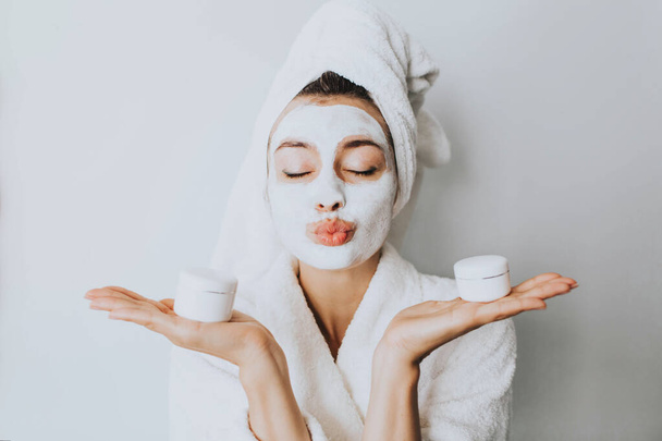 woman has fun with a facial mask.Young girl with facial mask, holding bottles of cream  looking at camera over white background. Cosmetic procedure. Beauty spa and cosmetology.Spa Facial Mask. Spa day - Foto, imagen