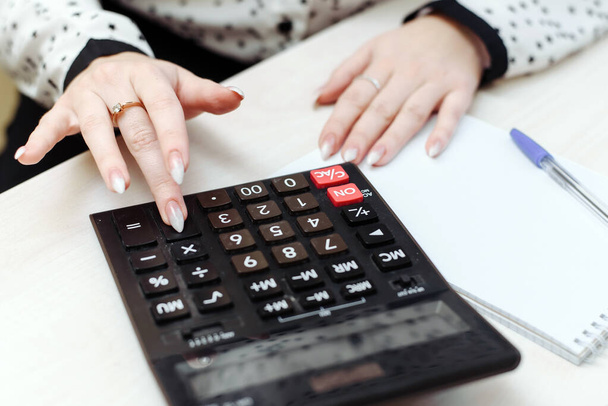 Egy nő számológéppel számolja a költségeket, bevételeket, kiadásokat. A családi költségvetés elosztása. Az üzletasszonyok könyveléssel foglalkoznak. - Fotó, kép