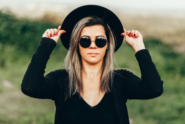Portrait of elegant woman wearing fedora hat and sunglasses outdoors - Фото, зображення