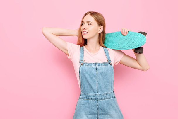 Portrait of a stylish attractive girl smiling and holding a skateboard isolated on a pink background in the Studio - Zdjęcie, obraz