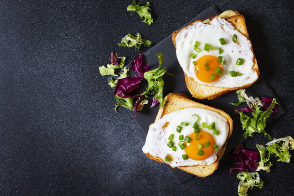 Sandwiches with ham, cheese and eggs. Traditional French croque-madame sandwiches served with lettuce leaves on a black plate. Popular French cafe meal. Black background. Top view. Space for text. - Photo, Image